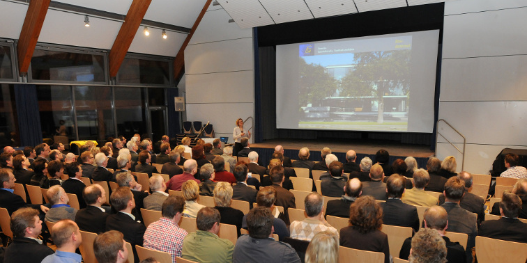Veranstaltungssaal mit Publikum, vor der Bühne (im Hintergrund eine Präsentations-Leinwand) hält Erste Bürgermeisterin Noller eine Rede