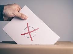 Wahlunterlagen werden per Hand in eine Wahlurne eingeworfen