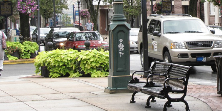 Straße in York mit Passanten und Autos, im Vordergrund: eine Parkbank