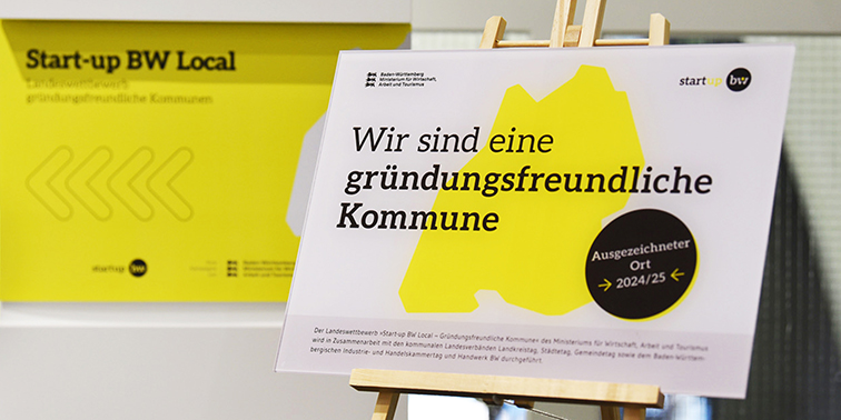 Themen-Special: Gründungsfreundliche Kommune Plakat mit der Aufschrift „Wir sind eine gründungsfreundliche Kommune – Ausgezeichneter Ort 2024/25“ im Rahmen des Wettbewerbs „Start-up BW Local“