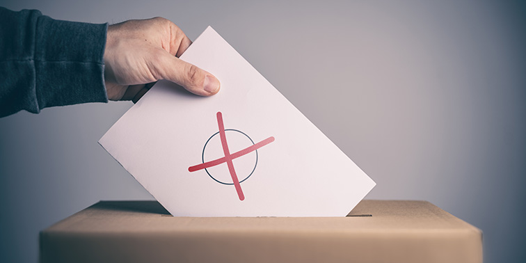 Wahlunterlagen werden per Hand in eine Wahlurne eingeworfen