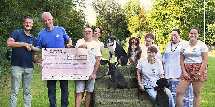 Eine Personengruppe mit Hunden bei einer symbolischen Scheckübergabe