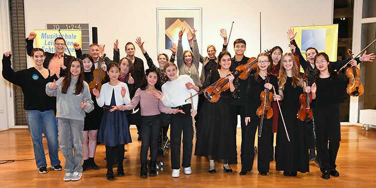 Gruppe von jungen Musikerinnen und Musikern mit Streichinstrumenten, die lächelnd und mit erhobenen Armen für ein Foto posieren