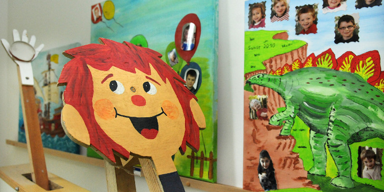Bestens betreut und gefördert Kindertageseinrichtung von innen mit Pumuckl-Spielzeug und bunten Fotos an den Wänden