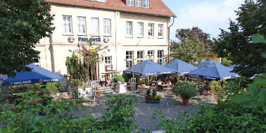 Biergarten im Freien mit blauen Sonnenschirmen, umgeben von grünen Bäumen